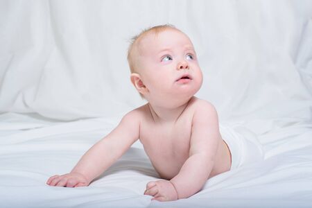 Baby on her tummy. Looking up with surprised expression. White backgroundの写真素材