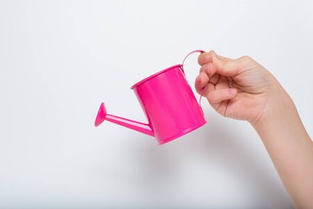 Small pink watering can in a children's hand on a light background.の写真素材