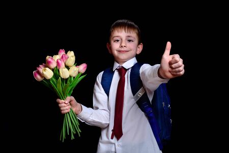 Schoolboy in a shirt with tie and school bag holding a bouquet of tulips. Isolated on black backgroundの写真素材