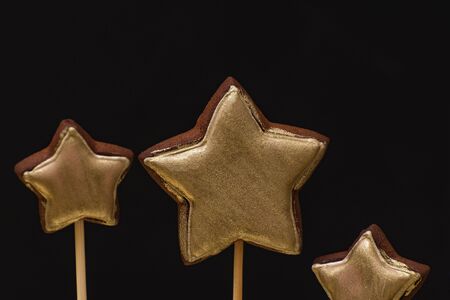 Gold colored gingerbread cookies on a stick on a black background.の写真素材