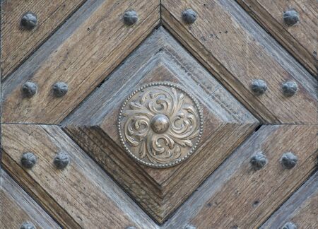 Old shabby bronze circle with a beautiful ornament on a wooden doorの写真素材