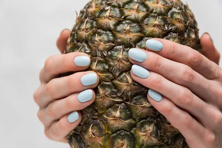Neat manicure on short nails. Blue gel polish. Pineapple in hands . Close upの写真素材