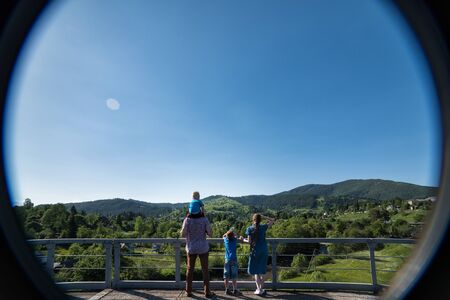 Family with children standing on the observation deck on nature background. Photo through the...