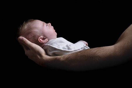 Baby in the arms of his father. Birth concept. Black background side view. Isolated.