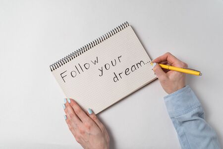Motivational inscription in notebook Follow your dream. Female hands writing in notepad. White background.の写真素材