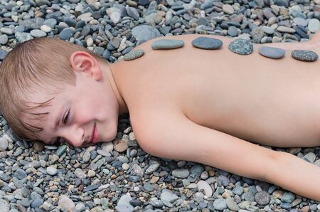 Child boy laying on the pebbles. Massage stones, rest and relaxation.の写真素材