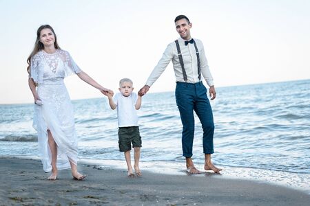 Young couple with a child walks on the beach. Beautiful family walking on the beach of ocean.の写真素材