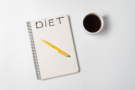 Cup of coffee, pen and a notebook title Diet. White background directly aboveの写真素材