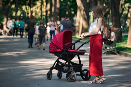 Young mother walking in the Park with a pram. Motherhood pfrenthood concept.の写真素材