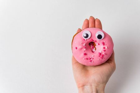 Doughnut with funny face and huge eyes lying on female hand on a white background.の写真素材