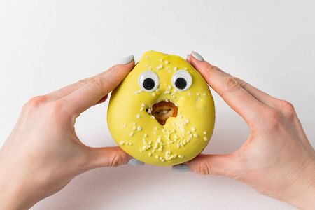 Two hands holding funny donut with huge eyes on white background. doughnut with face.