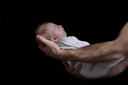 Male hands holding a baby. Infant sleeping. Black background. Side view, isolated.の写真素材