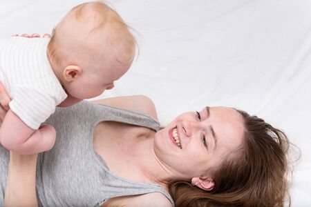 Mother with cute baby lying on bed. Mom and infant. Motherhood and parenthoodの写真素材