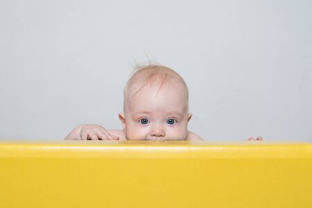 Playful surprised baby peeking out of playpen. Happy childhood.の写真素材