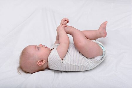 Portrait of a cute 3 months baby lying on bed. Newborn lies on his back and played foot.