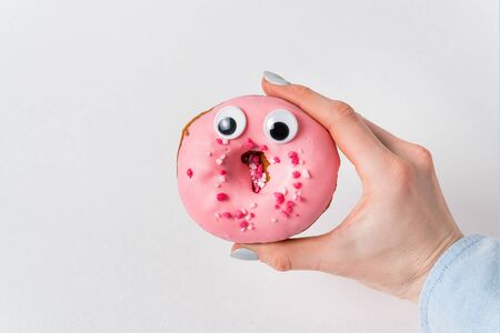 Female hand holding pink donut with huge eyes and surprised funny face on white background.の写真素材
