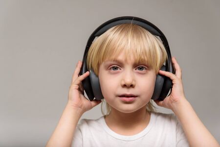 Blond boy teenager with headphones on light background. Teenager listens to music. Portrait.