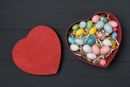 Top view of red Heart shaped box with colorful Easter eggs. Black background. Happy Easter.