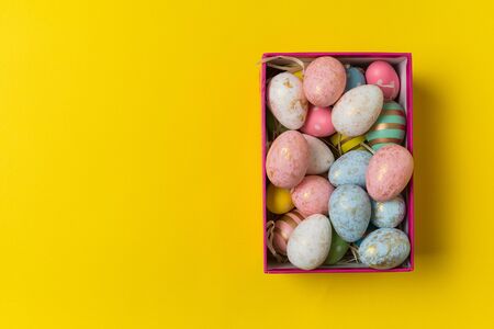 Top view of box with Easter eggs on bright yellow background. Holiday eggs.