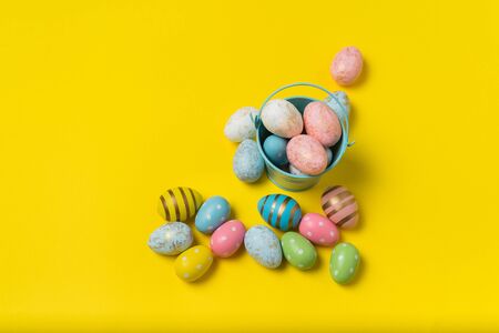 Bucket with colorful Easter eggs on bright yellow background. Many multicolored festive eggs.