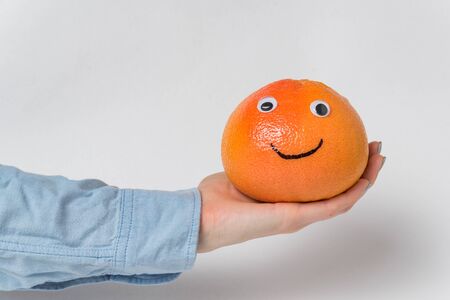 grapefruit-smiley with funny face rests on palm on white backgroundの写真素材