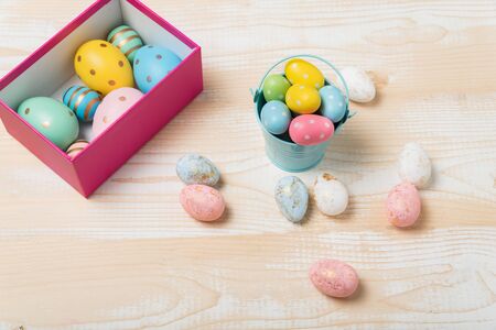 Box and bucket with colorful Easter eggs. Wooden background