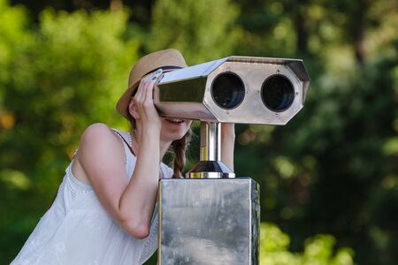 Young girl looking through tourist telescope on Park background.の写真素材