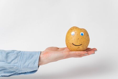 Funny potato with Googly eyes and smile lies in palm. White background.の写真素材