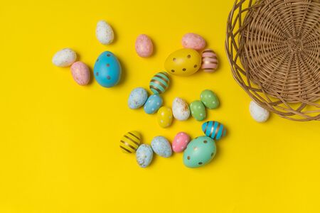 Many colorful Easter eggs near basket on yellow background. Top view of festive eggs.の写真素材