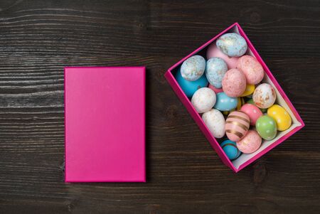 Pink box full of colorful Easter eggs. Dark wooden background. Top view.