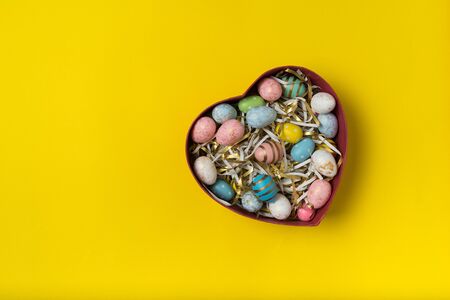 Heart shaped box with colorful Easter eggs. Yellow background. Happy Easter.