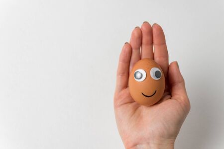 Funny egg with face lies on female hand on white background. Food with Funny Faces