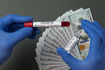 Doctor holding positive blood test for coronavirus and vial of vaccinal for Covid-19. Price for cure, medical gloves.の写真素材