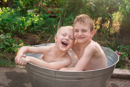 Two brothers bathing in basin ioutdoors and laughing. Weekend in village.