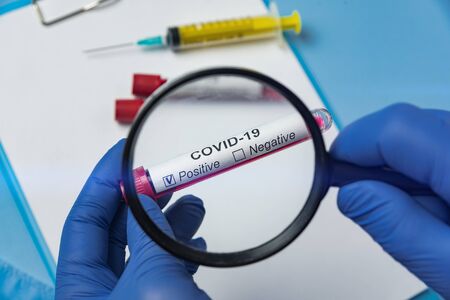 Positive blood test for Covid 19 and a magnifier in the hands of a medic. Biological sample with label Covid-19.の写真素材