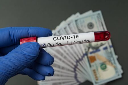 Hand in medical glove holding test tube with blood Covid-19. Money on background. Price analysis coronavirus.の写真素材