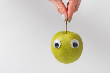 Fingers holding Apple with funny face. Apple on white background.の写真素材