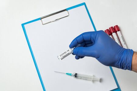 Doctor holds vial of vaccine coronavirus on background of syringe and clean sheets of paper