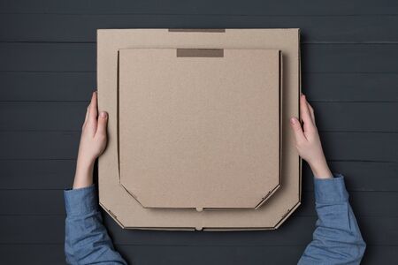 Pizza boxes in children's hands on black background. Top view. Copy space