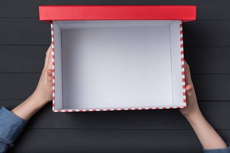 Open empty red box in children's hands on black background. Top view