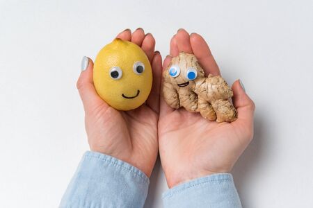 Lemon and ginger with funny faces lie on palms. White background. Healthy products.