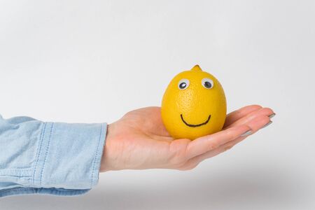 Funny lemon-smiley with Googly eyes lying on palm on white background.の写真素材