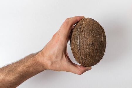 Men's hand holds a coconut on a white background. Man power concept.の写真素材