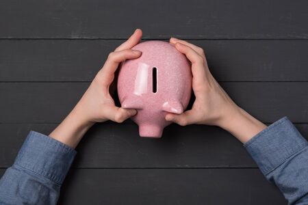 Child's hands holding piggy bank on black background. Top view. Crowd funding and savings concept.の写真素材