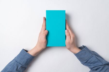 Child holds rectangular blue box on white background. Top view. Gift for child.