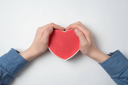 Top view of child's hand holding a small box in the shape of heart. Gift for momの写真素材