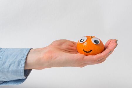 Sweet tangerine with funny face rests on palm on white background. Mandarin character.の写真素材