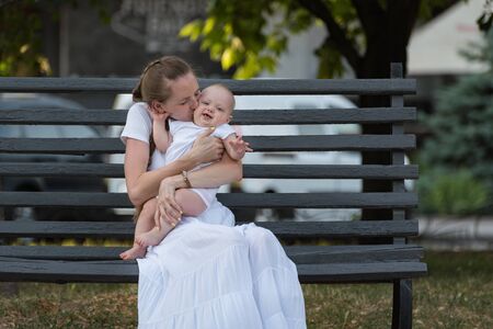 Portrait of happy mother with cute little baby sitting on bench in Parkの写真素材