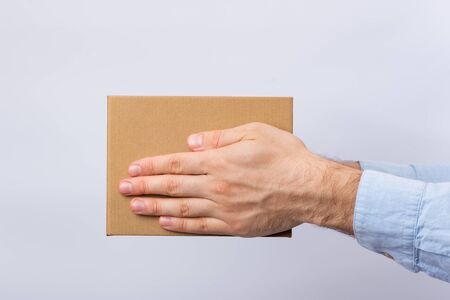 Square cardboard box in male hands. Delivery of parcels. Side viewの写真素材