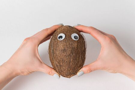 Female hands holding brown coconut on white background. coconut with Googly eyes.